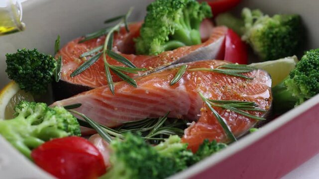 Cooking process. Salmon steak fish seafood with rosemary, broccoli and cherry tomatoes in baking pan. pouring olive oil