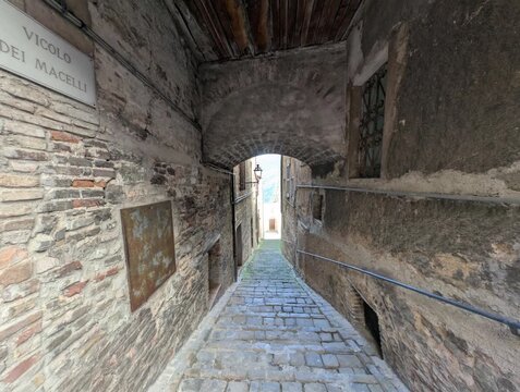 Vicolo stretto tra edifici storici in pietra, con archi, finestre e pavimentazione in ciottoli. Una scena suggestiva che cattura l&rsquo;atmosfera autentica di un borgo antico italiano