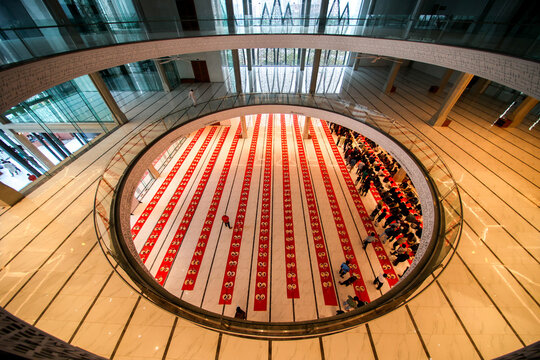 Dhaka, Bangladesh - 19 March 2025: View of a modern mosque's circular prayer hall, where vivid red and white mats contrast with sleek marble, bathed in light from above.