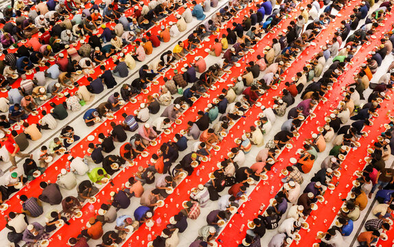 Dhaka, Bangladesh - 19 March 2025: View of a vibrant communal meal where countless individuals gather in neat rows on striking red carpets, sharing food in a powerful display of unity.