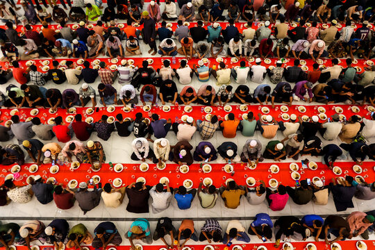 Dhaka, Bangladesh - 19 March 2025: View of rows of people in diverse attire bowing over meals on a vibrant red carpet, creating a striking pattern of communal gathering.