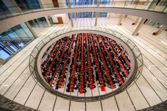 Dhaka, Bangladesh - 19 March 2025: View of a large corporate event in a circular atrium, vibrant red tables packed with dark-suited attendees under modern architecture.