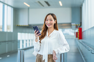 Asian Businesswoman holding smartphone and smiling at camera in airport walkway © StockPhotoRepublic