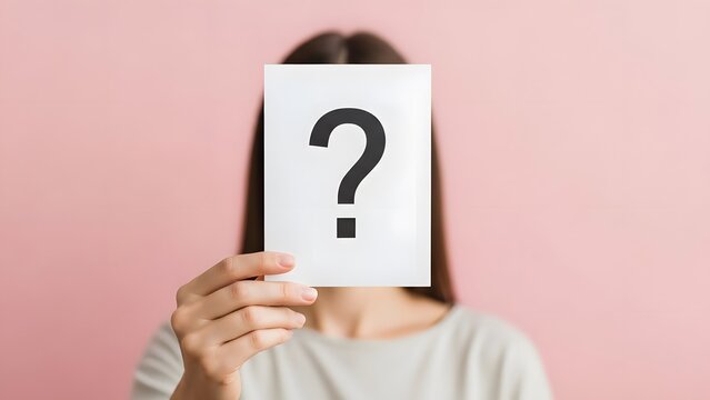 Person holding paper with question mark covering face. Curiosity and anonymous identity. Woman hiding behind a white card with black symbol on pink background
