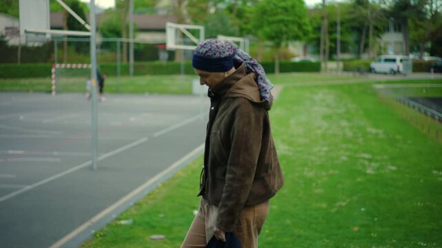 Woman undergoing cancer treatment walking near playground basketball court observing children symbolizing resilience strength hope and normal life during recovery