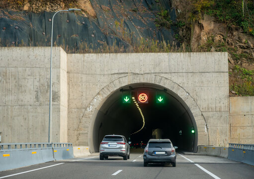 Highway tunnel entrance with moving cars, speed limit sign, traffic lanes and concrete infrastructure, covering road safety, transport engineering and modern mobility.