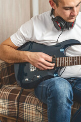 Obraz premium A young man with a smartphone while holding an electric guitar. Musician sitting on a couch and holding guitar
