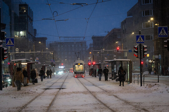 Tallinn, Estonia - 03 January 2025: View of a snow-blanketed city street at dusk, with a tram and pedestrians under the warm glow of urban lights.