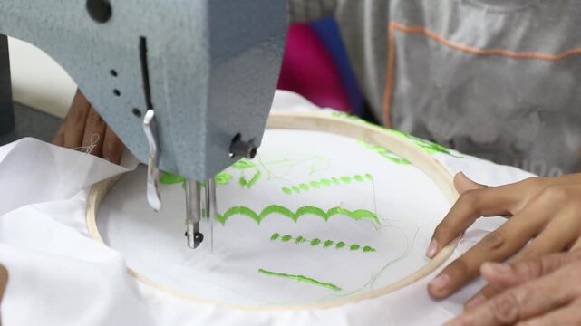 A detailed close-up shot of an industrial sewing machine being used for hand-guided embroidery. The video captures the rapid motion of the needle as it stitches intricate green scalloped and patterns.
