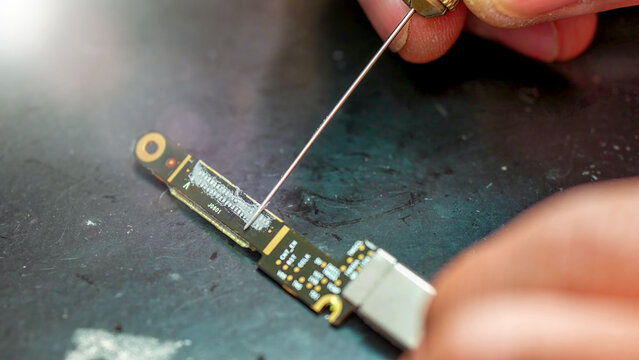 Close-up technician cleaning laptop connector in electronics repair workshop