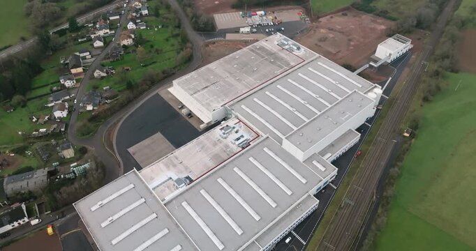 Aerial drone shot rotating around a modern white logistics center adjacent to rural landscape and houses