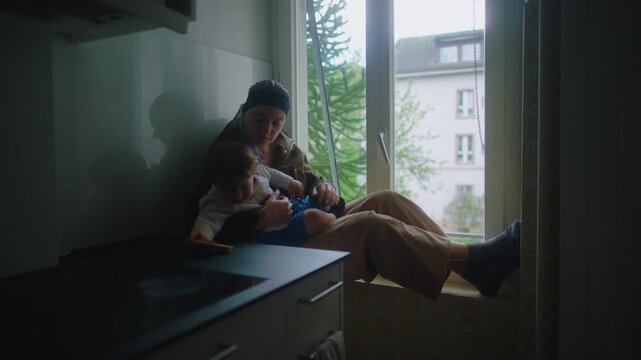 mother with cancer sitting with child on window ledge in apartment during chemotherapy sharing quiet moment of connection support and resilience in challenging treatment recovery phase