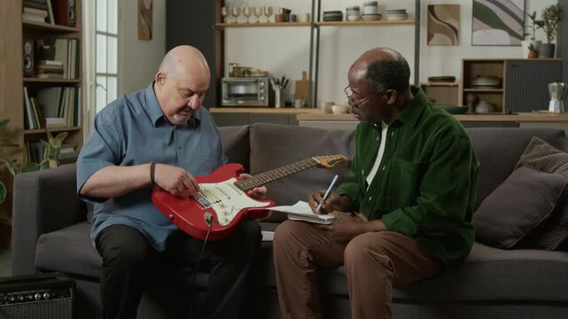 Medium shot of male music teacher explaining electric guitar parts to senior Black man taking notes during lesson Great for beginner guitar course promotion