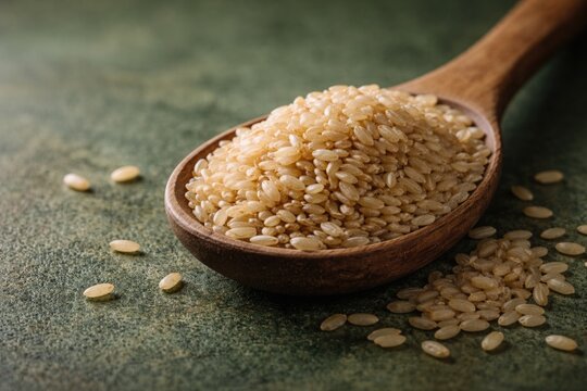 Close up image of brown GABA rice resting in wooden spoon on green textured surface with copy space