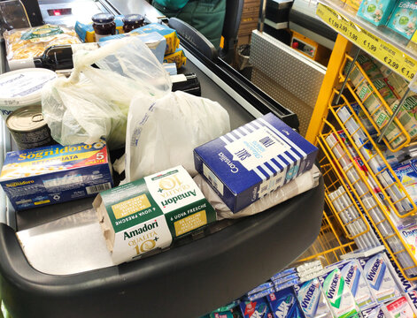 Rome, Italy - March 29, 2026: Grocery cart filled with various food items including pasta, eggs, and packaged goods at a supermarket checkout counter