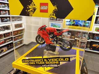 Fototapeta premium Rome, Italy - March 29, 2026: LEGO motorcycle model displayed in a glass case with promotional graphics and colorful shelves of toy sets in the background
