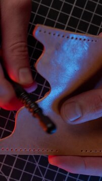 Vertical 4K ASMR video of a craftsman using an ebonite smoothing tool to burnish the edge of a leather piece.