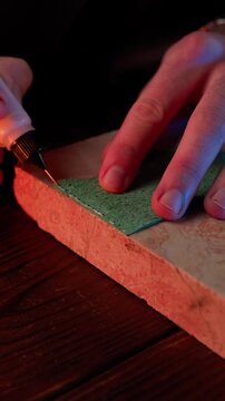 Vertical 4K ASMR video of a craftsman spreading white glue on green leather with a plastic spatula.