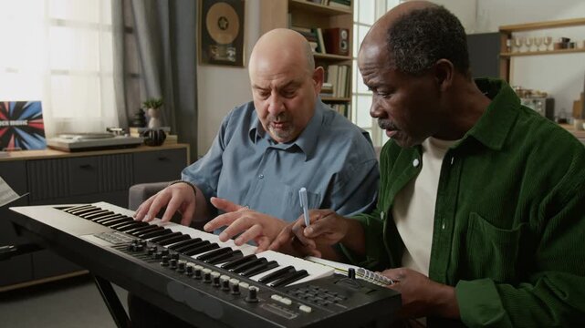Middle aged male teacher explaining notes on keyboard to senior Black man taking notes during music lesson Useful for educational platforms or learning focused content