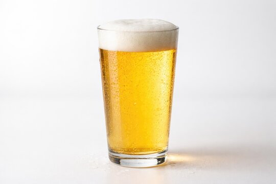 Crisp pale lager beer in transparent glass on plain white surface