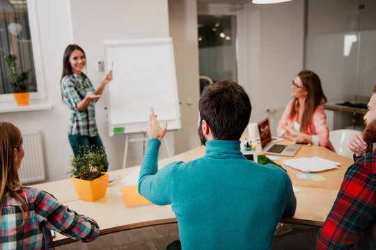 Colleagues in a casual business meeting with a woman presenting at a flipchart and team members discussing ideas around a table