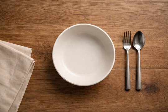 Flat lay showing a blank bowl resting on a grained wood dining table