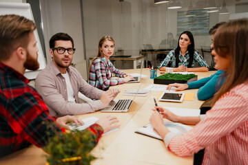Obraz premium Young team of coworkers having a business meeting around a conference table collaborating on laptops and documents in a modern office