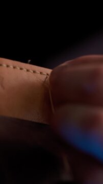 Vertical 4K ASMR video of a craftsman tightening the final knot after hand stitching a leather product.