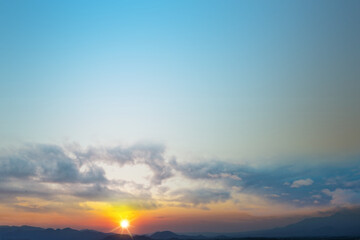 Fototapeta premium A breathtaking view of the sun setting or rising over a distant mountain range under a vast blue sky with soft clouds, creating a peaceful natural landscape