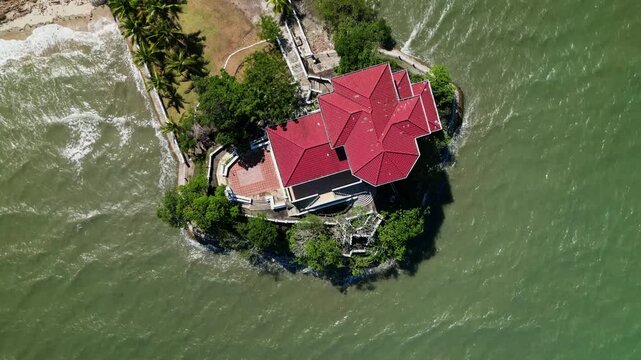 Aerial top-down shot of a seaside mansion on a small islet with surrounding ocean and tropical landscape in Guimaras, Philippines.
