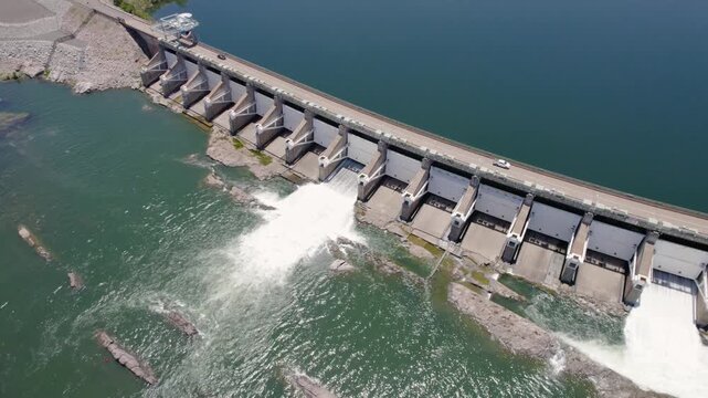 Car Crossing Diversion Dam Over River, Water Flowing Through Spillway Gates and Reservoir Landscape - Aerial Drone Shot