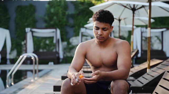 Young man squeezing sunscreen onto hand, preparing to apply it for skin protection while relaxing at a luxurious poolside resort during summer