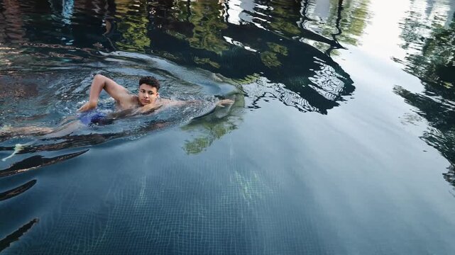 Young black boy swimming laps in a dark infinity pool, creating ripples and reflections while exercising and enjoying a summer day