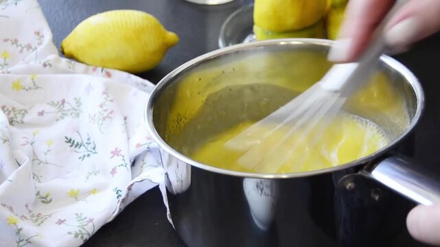 Close-up of hands whisking lemon curd in a saucepan with smooth creamy texture forming. Homemade dessert preparation with fresh lemons and baking process.