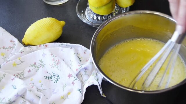Close-up of hands whisking lemon curd in a saucepan with smooth creamy texture forming. Homemade dessert preparation with fresh lemons and baking process.