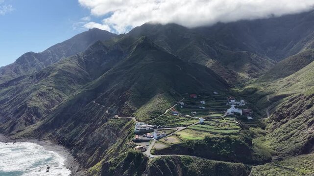 Aerial drone view of waves hitting rocky coastline, turquoise ocean and natural seascape. Anaga Rural Park.Aerial drone footage of ocean waves breaking against a rugged rocky coastline with clear tur
