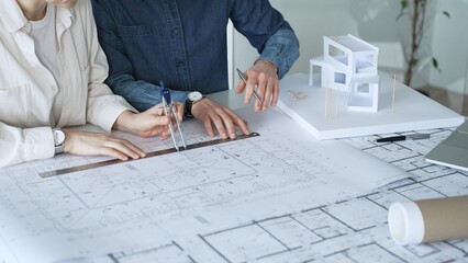 Architects working together, developing a building design by assembling a scale model and reviewing detailed blueprints, symbolizing teamwork, planning, and architectural creation © volha_r