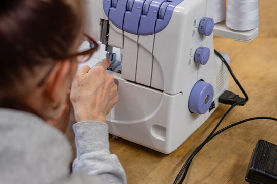 Female sewing enthusiast operates a serger machine, focusing on threading and fabric manipulation in a cozy sewing cafe environment with wooden tables