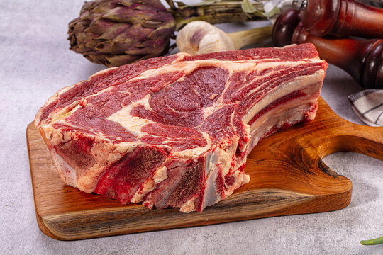 Raw beef rib eye steak on wooden board. Fresh artichoke, garlic, bay leaves, green onions, pepper mills. Gourmet cooking ingredients