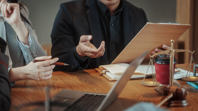 Business meeting scene with professionals discussing documents at a wooden table, laptop, clipboard, scales of justice and gavel visible