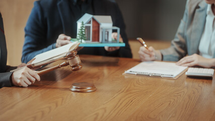 Fototapeta premium Gavel and house model on table during real estate legal meeting, close-up of hands signing documents, property auction or contract concept.