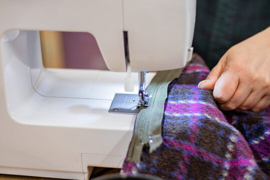 Sewing machine in use with a person's hand guiding fabric through the presser foot, showcasing a colorful plaid pattern and a close-up view of the sewing process