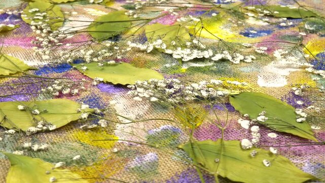 Flat dried flower arrangements. Dried pressed gypsophila paniculata    flowers and camellia leaves lie on the beige burlap cloth with abstract painting, background, side view 
