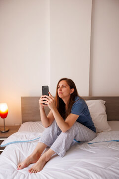 Bored woman surfing the net using smart phone in bed after waking up