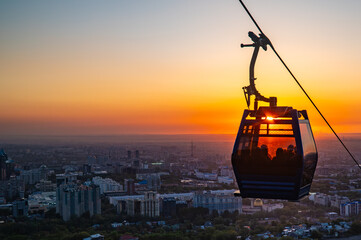 Cable car gondola over illuminated Almaty city skyline at dramatic orange red sunset dusk © Ployker