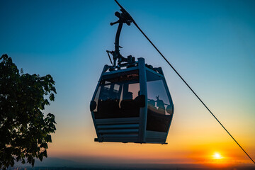Cable car gondola silhouette against dramatic vivid orange sunset with sun on horizon © Ployker