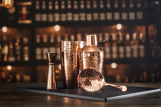 Shaker, jigger, strainer and mixing glass are on bar counter. Black Bar mat. Glossy surface. Classic accessories for bartender. Copper-colored bar accessories