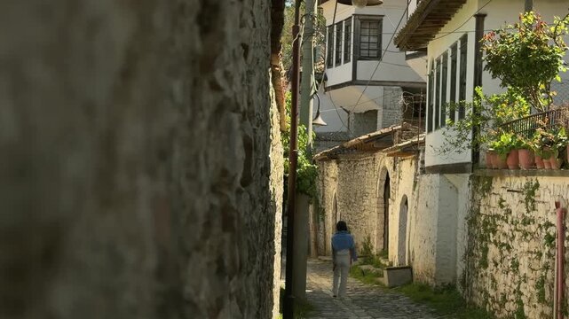 Woman tourist walk sightseeing old Gorica quarter residential district in Berat. Tiered Ottoman narrow old cobblestone streets in sunny summer day in Albania