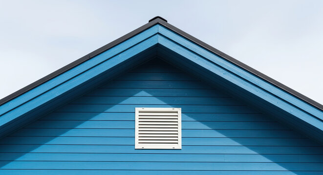 Blue wooden house gable with white ventilation vent under clear sky