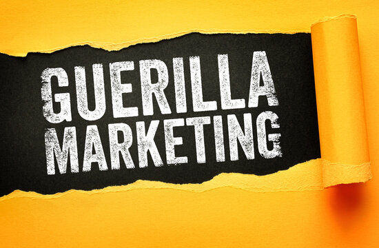 Guerilla marketing text shown behind a torn paper hole. Creative advertising strategy concept for business growth, unconventional promotion, and brand awareness tactics